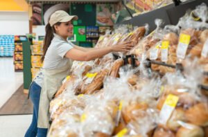 A grocery store clerk arranges bread on the bakery shelf.