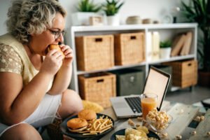 Overweight woman eating in her living room.