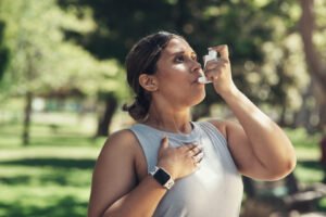 A young woman uses her asthma inhaler in the park.