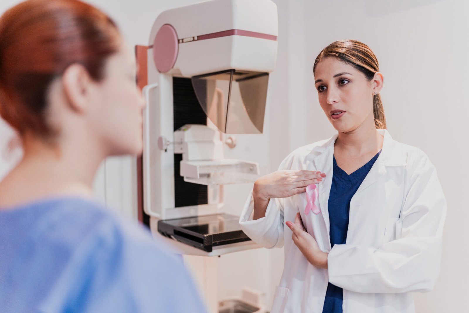 A patient and doctor talk beside a mammogram machine.