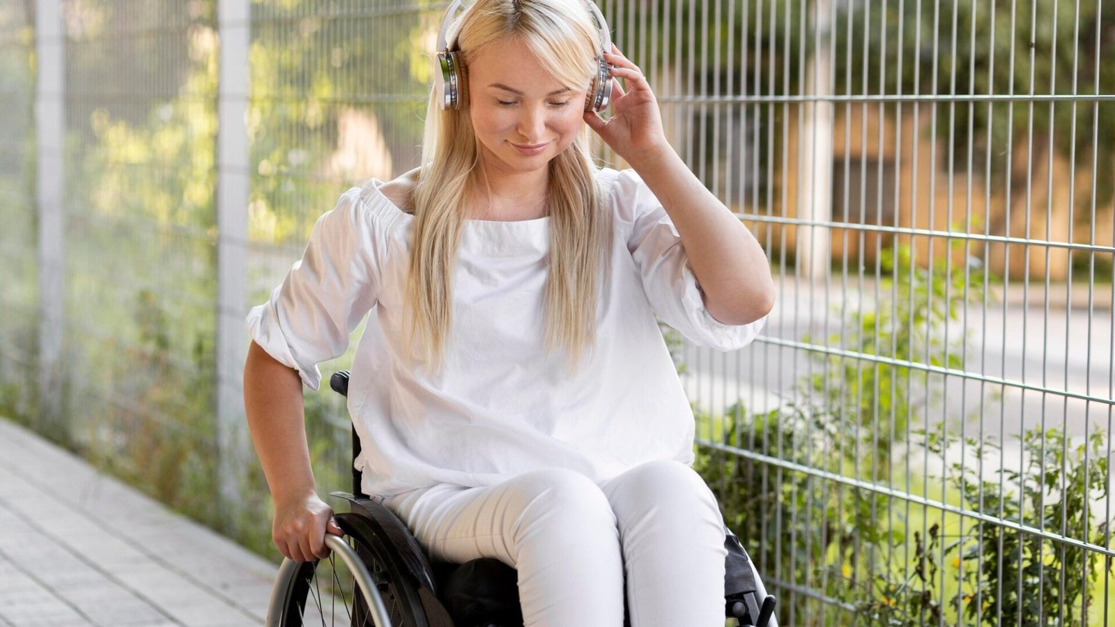 A young woman with MS sits in her wheelchair, listening to music on headphones.