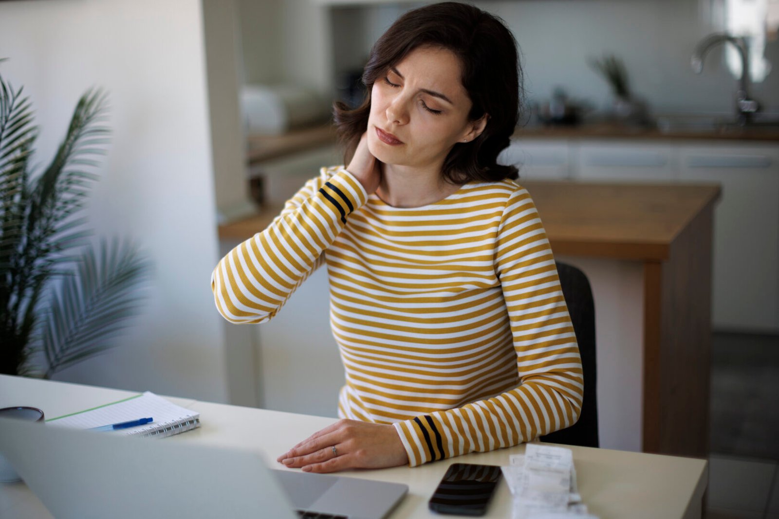 A woman sitting at her desk massaging her neck. She has fibromyalgia pain.